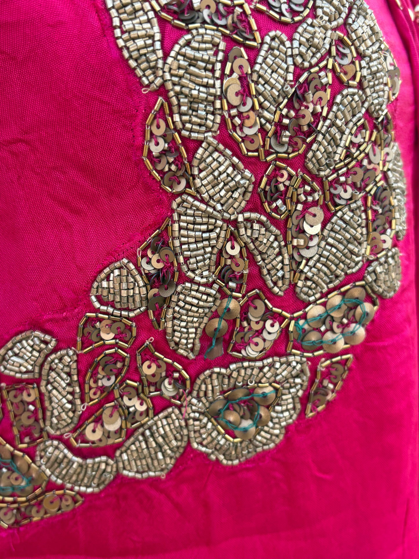 Close-up of a bright pink fabric garment featuring an ornate, detailed hand-embroidered and beaded floral pattern in metallic gold, silver, and multicolor sequins.